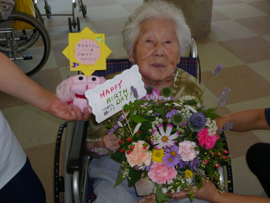 102歳のお誕生を祝ってもらい花束和抱くおばあさん