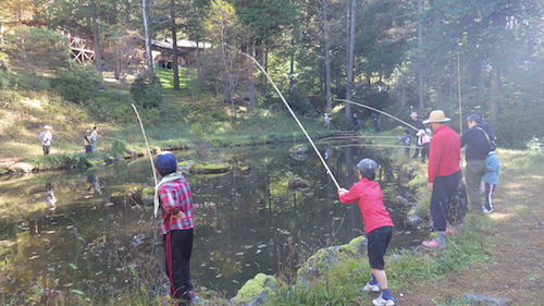 池で縄文釣り体験する子どもたちと大人