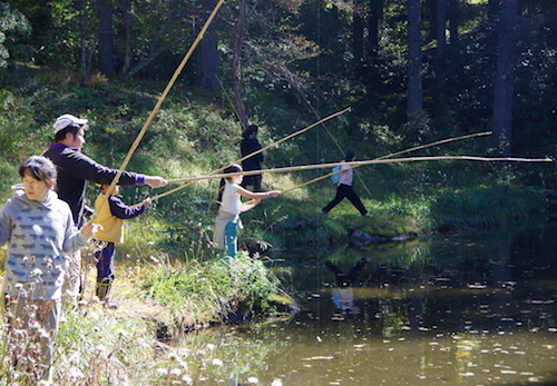 池で縄文釣り体験する3人の子どもと大人