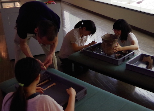 学生たちが土器などの遺物を手に取って観察している写真